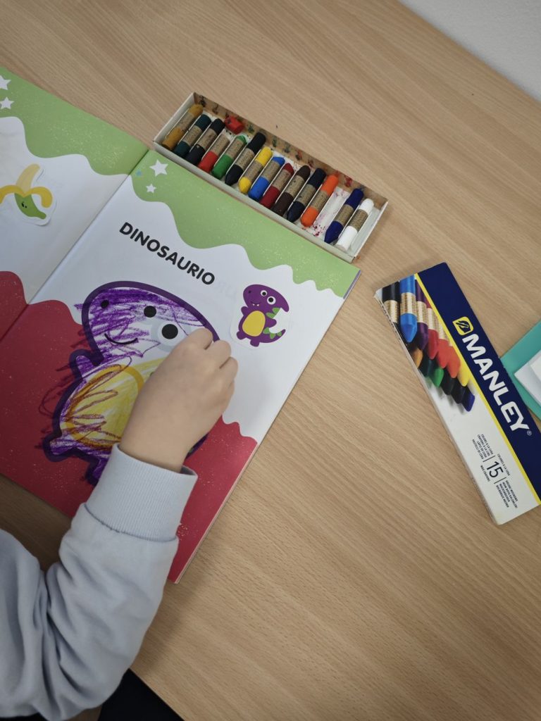 Mano de un niño coloreando un dinosaurio con ceras de colores