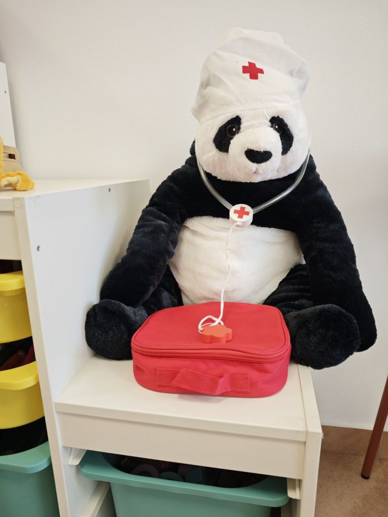 Peluche de panda con gorro de enfermero y un botiquín rojo en la consulta
