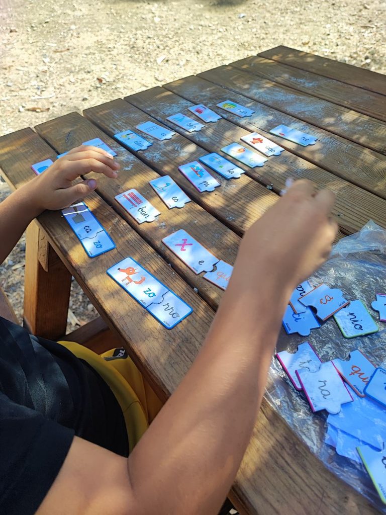 Niño formando sílabas con un puzle sobre una mesa de madera al aire libre